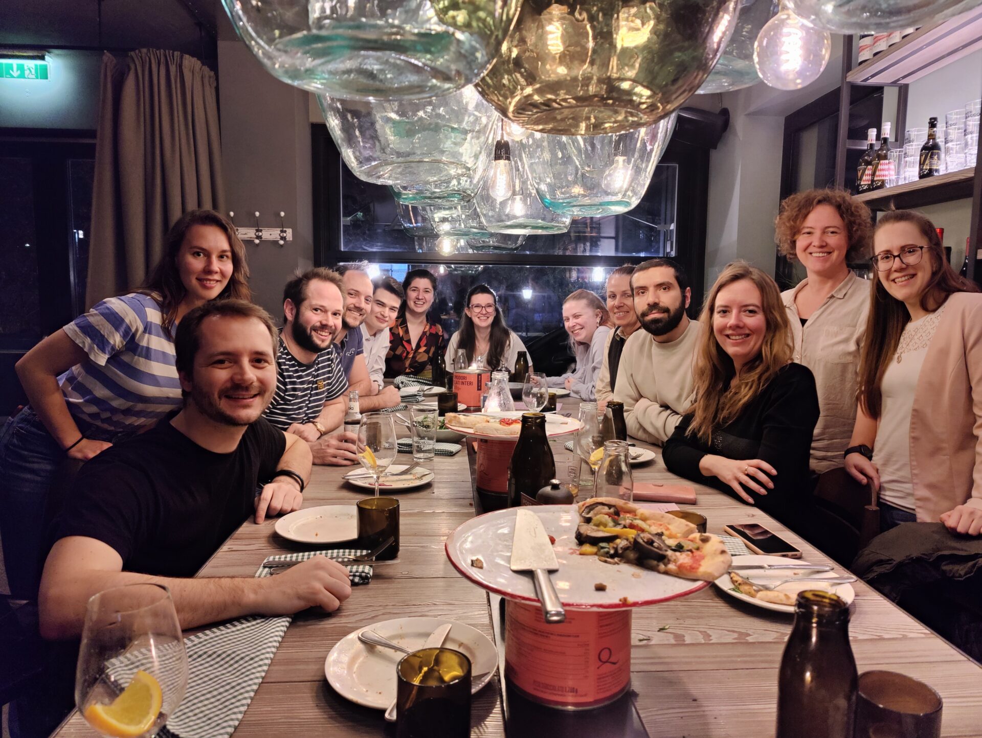 Gruppenbild der Mitarbeitenden rund um einen Tisch mit Pizza