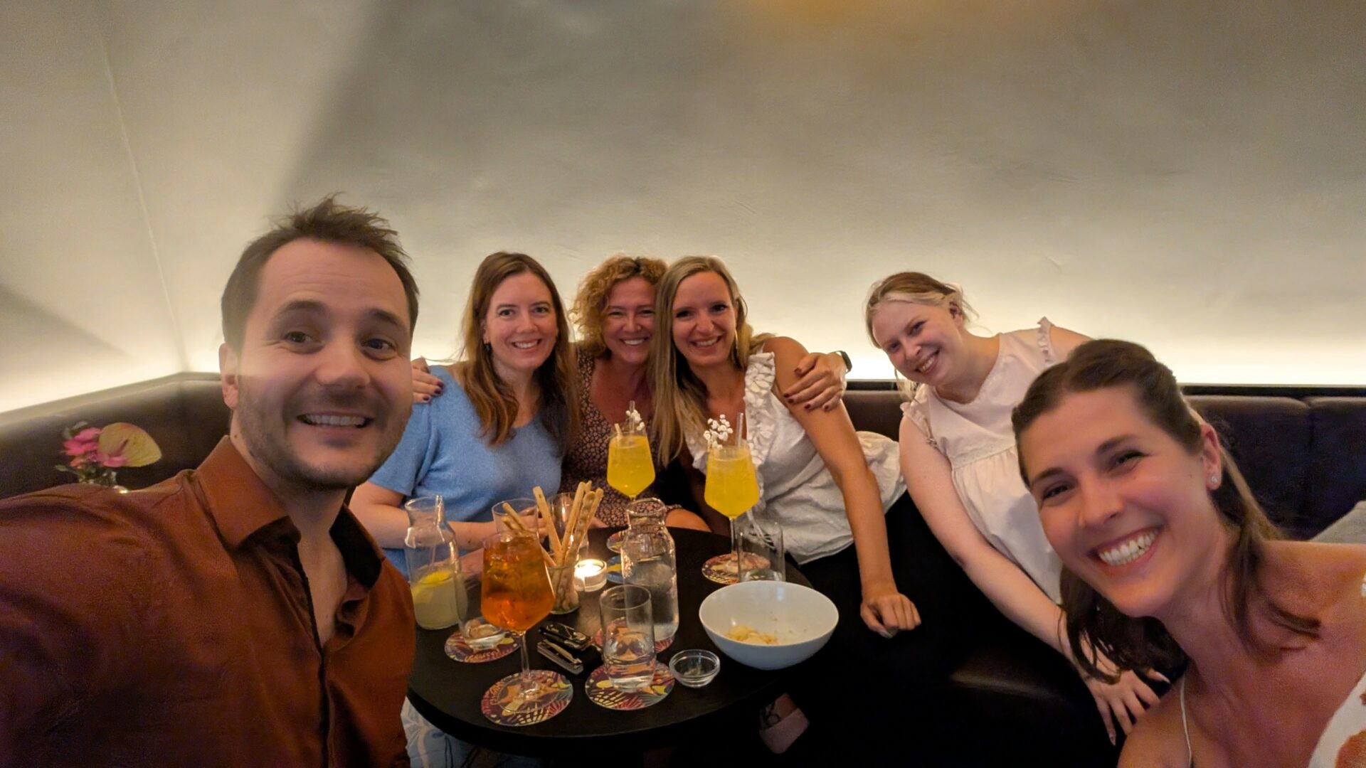 Gruppe von Menschen in einer Cocktailbar und in der Mitte steht ein Tisch mit Snacks und Getränken